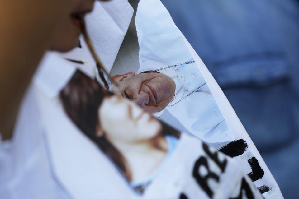 Reanta Grattani, who claims to be a friend of the Ornaldi family, wears a t-shirt bearing the pictures of Emanuela Orlandi and Pope Francis and a writing reading: I'm watching you from the sky, but you (referring to Pope Francis) please let them return my mortal remains to my mother, as they gather outside the Vatican, Saturday, July 20, 2019. The mystery of the 1983 disappearance of the 15-year-old Emanuela Orlando, daughter of a Vatican employee, took yet another twist Saturday as the Vatican formally opened two ossuaries discovered under a stone slab. The boxes of bones were found after the Vatican opened the tombs of two 19th-century German princesses in the cemetery of the Pontifical Teutonic College in hopes of finding the remains of Emanuela Orlandi. (AP Photo/Gregorio Borgia)