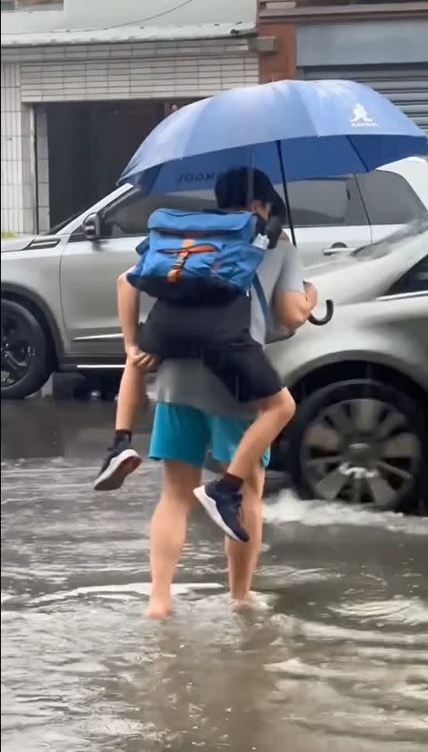 苗栗頭份豪雨狂炸，造成住家門口積水，一名慈父揹著兒子涉水上學。（圖／翻攝我是頭份人）