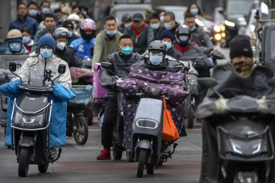 Commuters wearing face masks ride scooters along a street in the central business district in Beijing, Friday, Oct. 28, 2022. (AP Photo/Mark Schiefelbein)