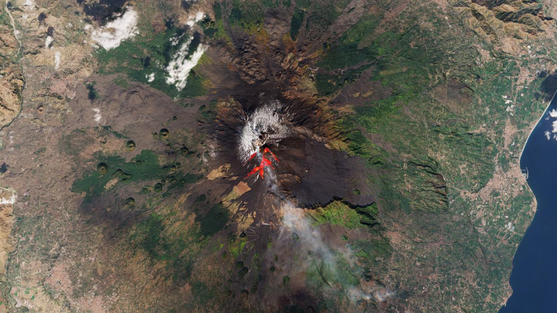  An aerial view of a volcano eruption. Slight bits of bright red lava are seen coming from the top of the volcano. 