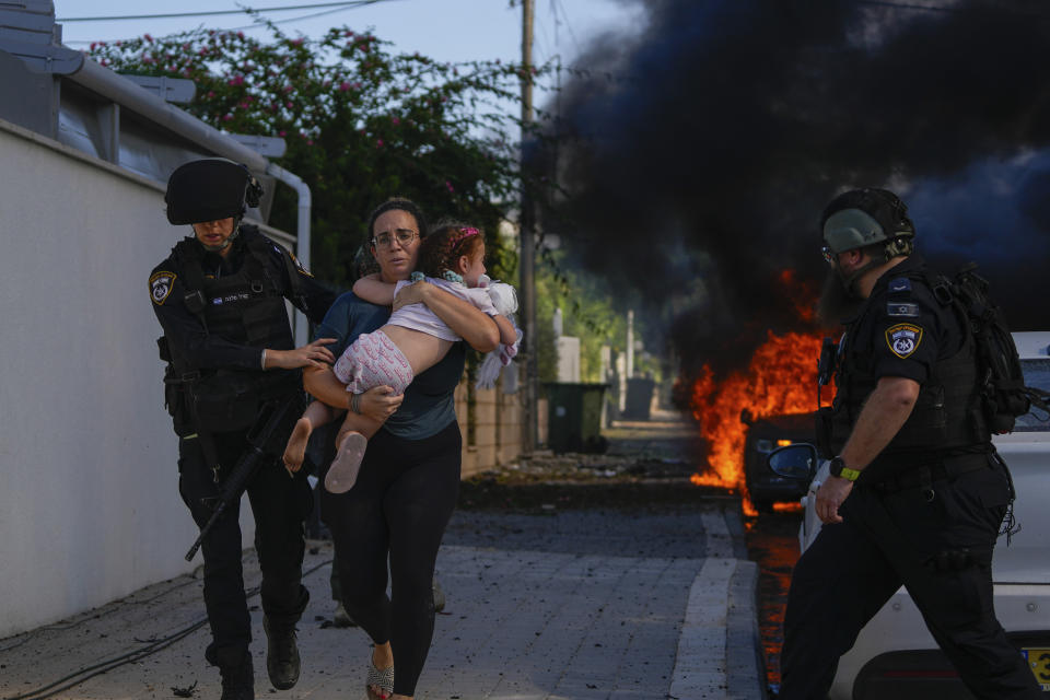 Police officers evacuate a woman and a child from a site hit by a rocket fired from the Gaza Strip, in Ashkelon, southern Israel, Saturday, Oct. 7, 2023. The rockets were fired as Hamas announced a new operation against Israel. (AP Photo/Tsafrir Abayov)