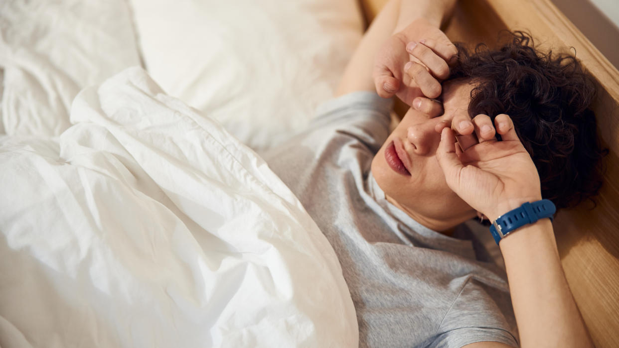  Person wearing sports watch waking up in bed and rubbing eyes 