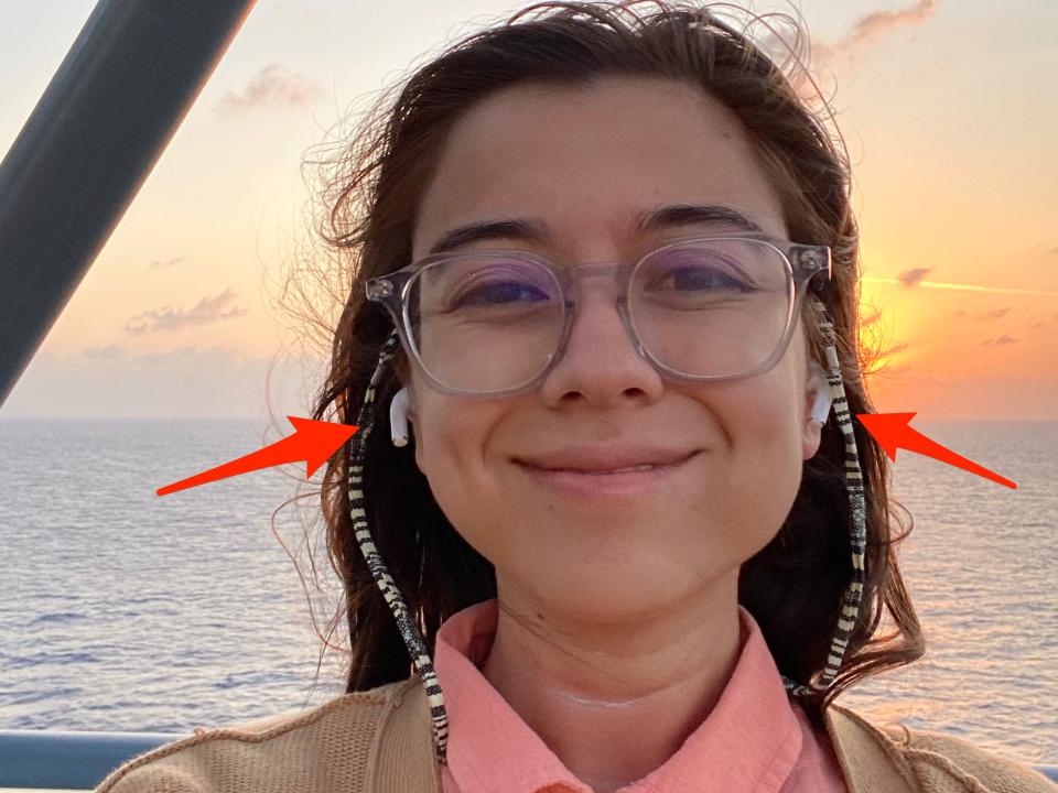 A selfie of the author with a sunset and the sea in the background, arrows point to eadbuds in her ears