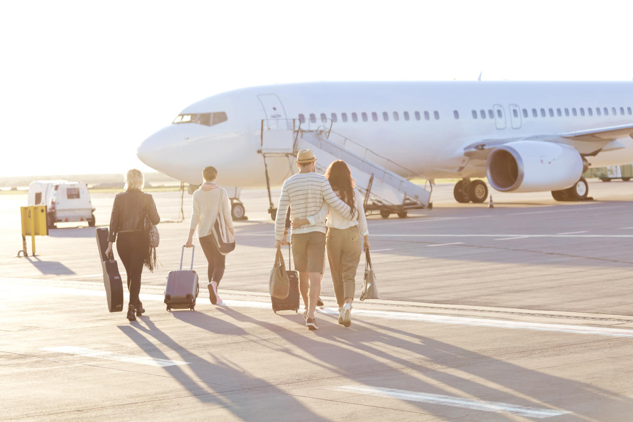 Rear view of flight passengers going towards the airplane. People boarding on the flight on airport runway.