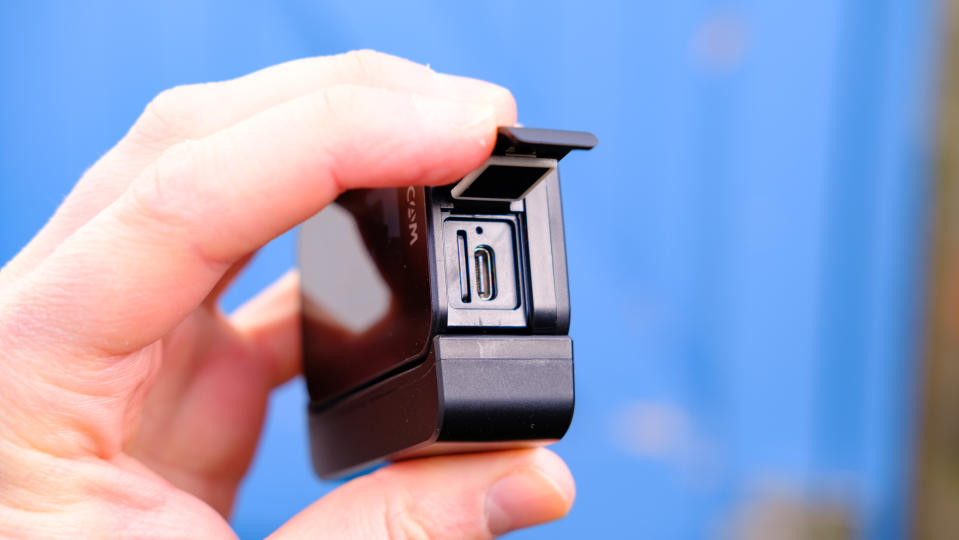 A photo of the SJCAM Sj20 being held up with the USB-C and card slots showing against a blue backdrop.