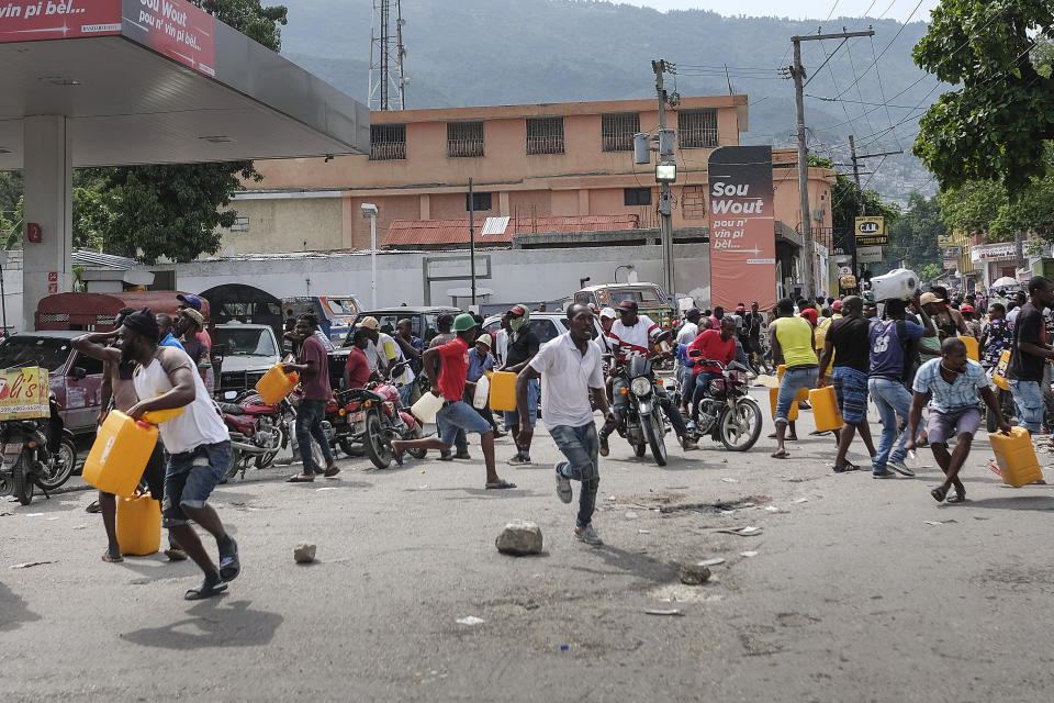 People run for cover as police shoot into the air to disperse a crowd threatening to burn down a gas station because they believed the station was withholding the gas, in Port-au-Prince, Haiti, Saturday, Oct. 23, 2021. The ongoing fuel shortage has worsened, with demonstrators blocking roads and burning tires in Haiti's capital to decry the severe shortage and a spike in insecurity. (AP Photo/Matias Delacroix)