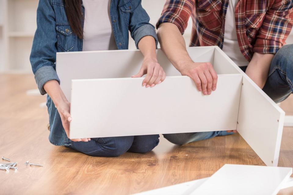 Two people put a piece of white furniture together.