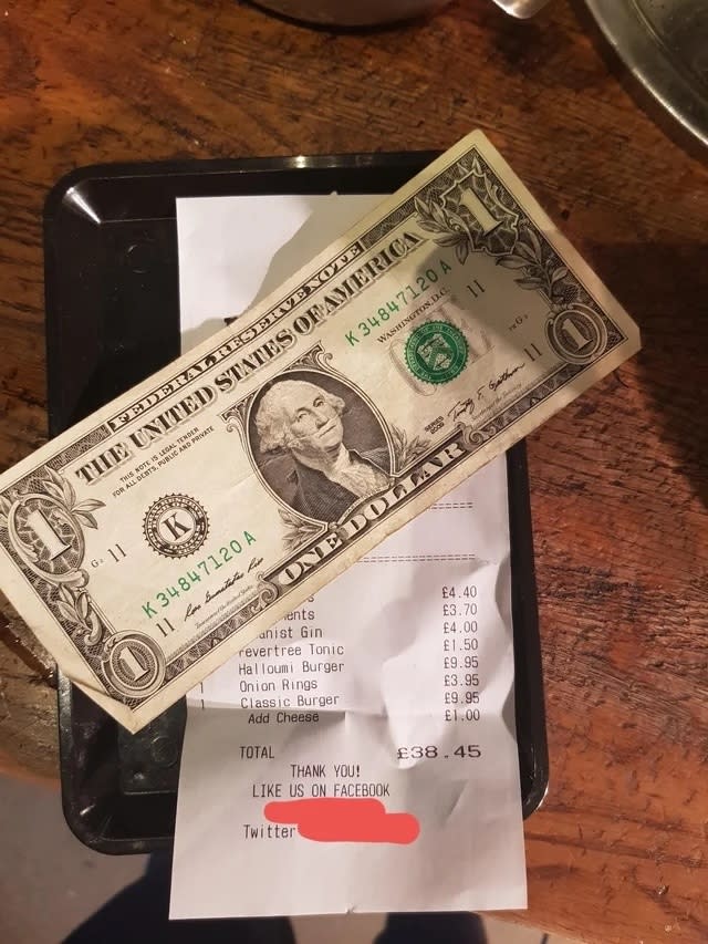A person's hand placing a US dollar bill on a restaurant receipt with a total amount written in British pounds