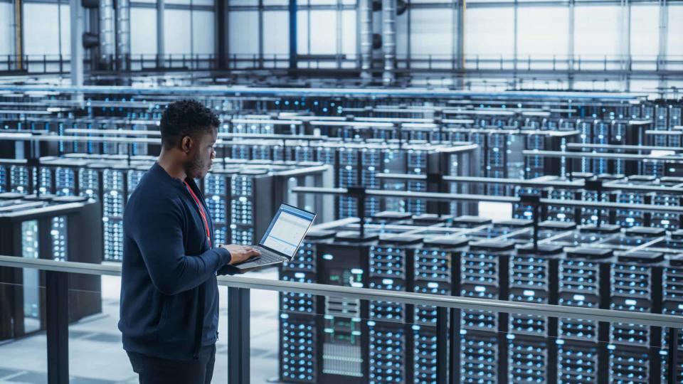 A data center engineer works on a laptop at a server farm.