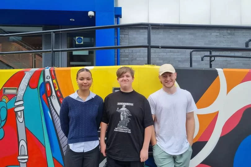 Three happy students standing in front of a technicoloured mural.