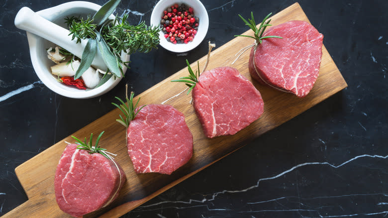 Raw filet mignon steaks on board with herbs