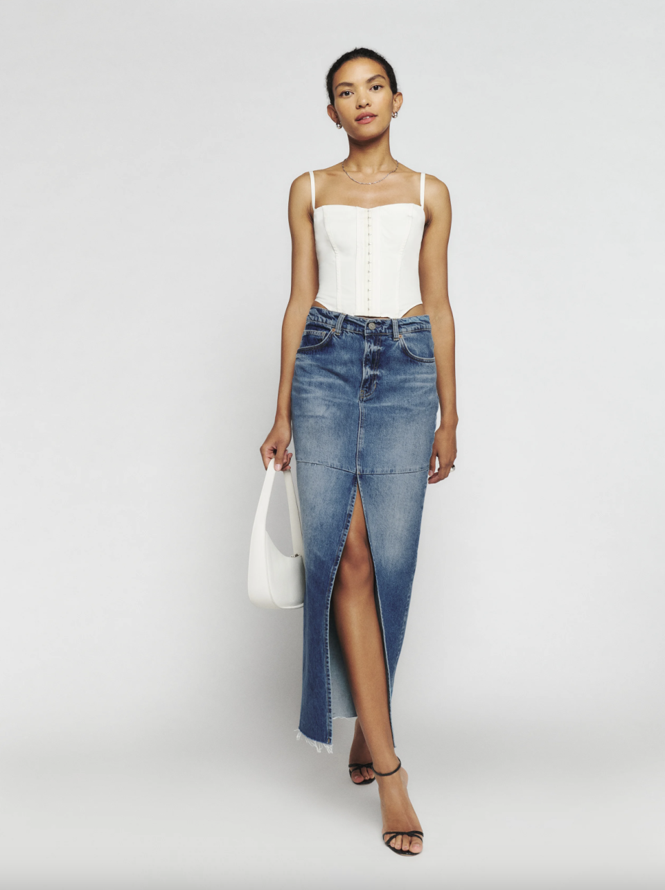 model wearing white corset top and long denim skirt with slit, Tazz Maxi Denim Skirt (Photo via Reformation)