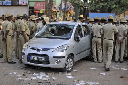 Policemen stand next to a damaged vehicle after a protest by garment workers in Bengaluru, India, April 19, 2016. REUTERS/Abhishek N. Chinnappa