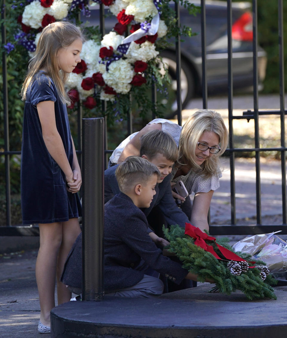 Tiffany Utterson, right, and her children, from left to right, Ella, 11, Ian, 10 and Owen, 8, place a wreath outside the gated community entrance to the home of George H.W. Bush Sunday, Dec. 2, 2018, in Houston. Bush is returning to Washington as a revered political statesman, hailed by leaders across the political spectrum and around the world as a man not only of greatness but also of uncommon decency and kindness. Bush, died late Friday at his Houston home at age 94, is to be honored with a state funeral at National Cathedral in the nation's capital on Wednesday, followed by burial Thursday on the grounds of his presidential library at Texas A&M.(AP Photo/David J. Phillip)