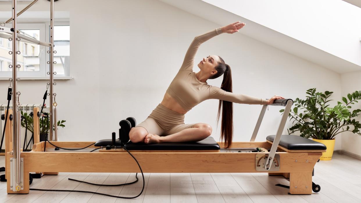  Woman in activewear on a reformer Pilates bed during Pilates class. 