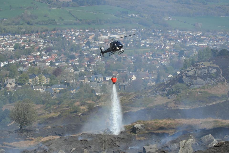 Firefighters use a helicopter to drop water as they tackle a large fire which is continuing to burn on Ilkley Moor (PA)