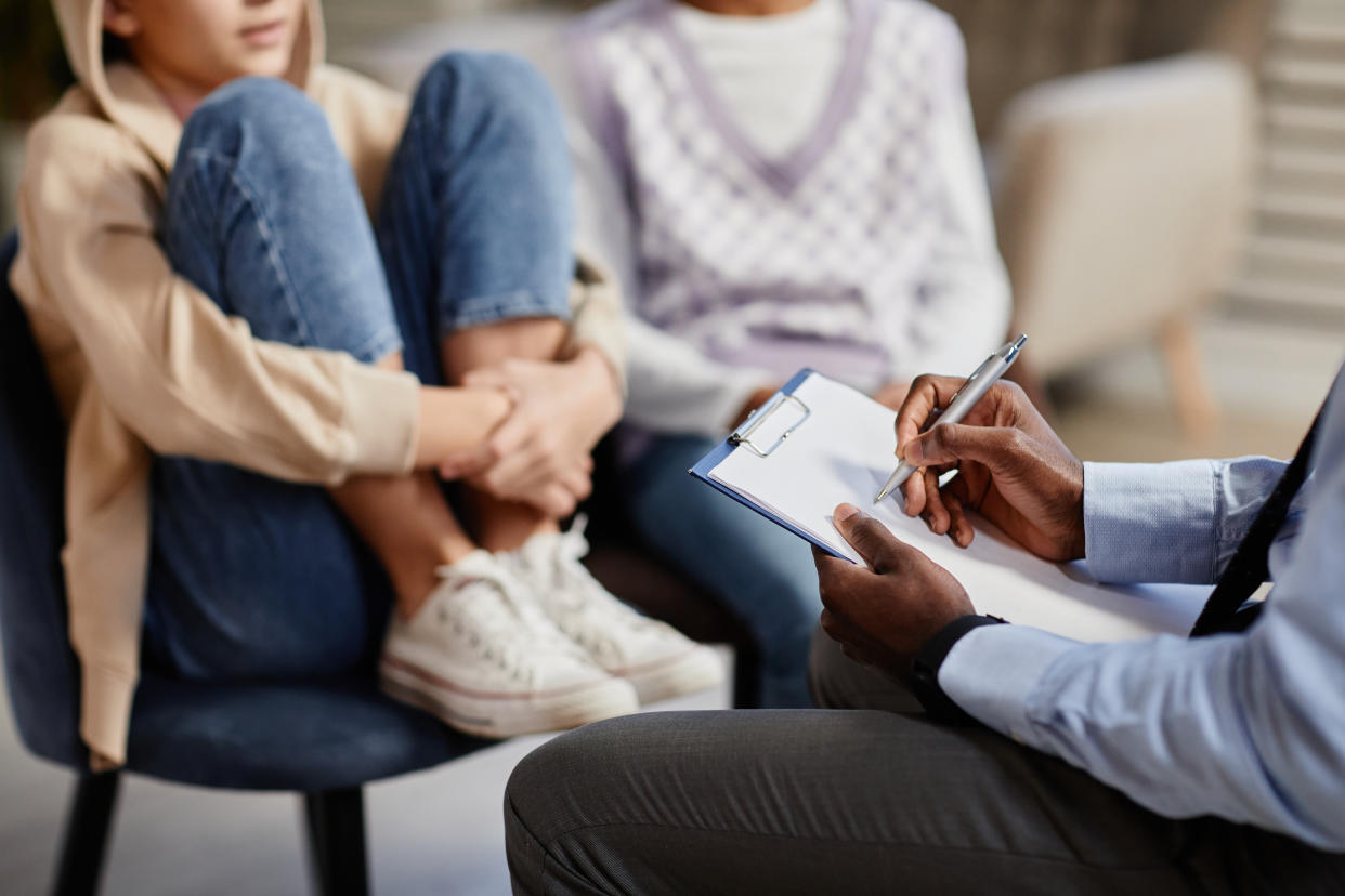 Close up of a therapist taking notes while talking with a teen and parent.