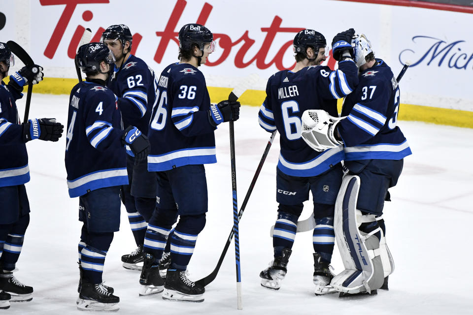 Winnipeg Jets goaltender Connor Hellebuyck (37) celebrates after his shutout against the Washington Capitals with Colin Miller (6) and other teammates after an NHL hockey game in Winnipeg, Manitoba, Monday March 11, 2024. (Fred Greenslade/The Canadian Press via AP)