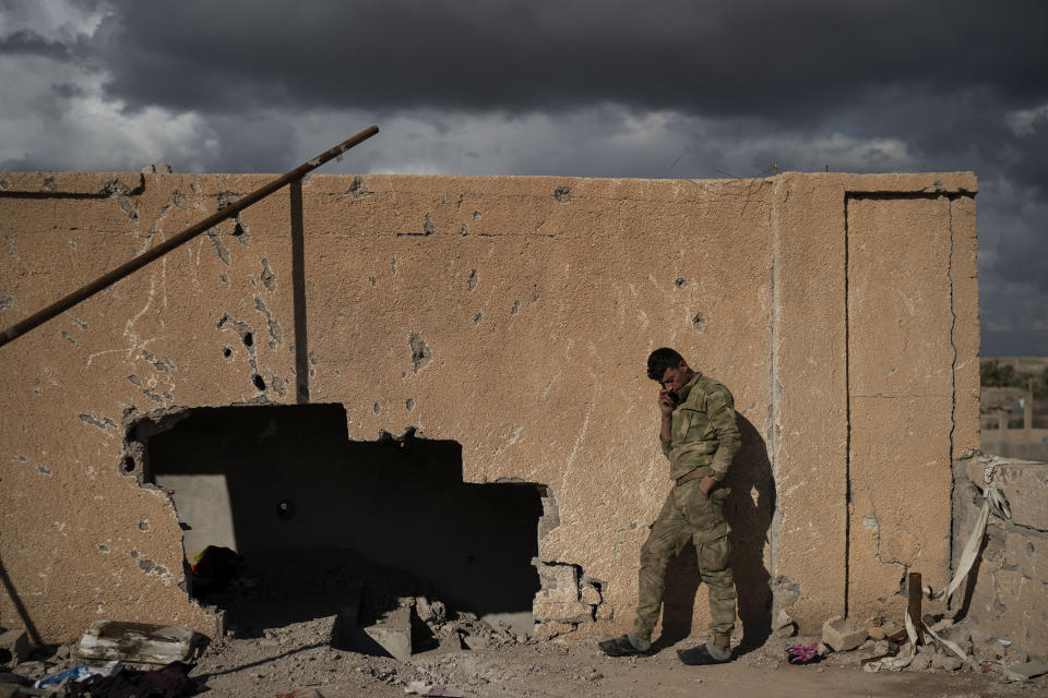 A U.S.-backed Syrian Democratic Forces (SDF) fighter talks on his phone from atop a building recently taken by SDF as fight against Islamic State militants continue in the village of Baghouz, Syria, Sunday, Feb. 17, 2019. Islamic State militants are preventing more than 1,000 civilians from leaving a tiny area still held by the extremist group in a village in eastern Syria, a spokesman for the U.S.-backed Syrian militia fighting the group said Sunday. (AP Photo/Felipe Dana)