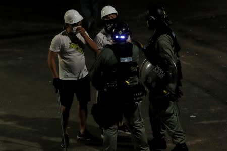 Men in white T-shirts and carrying poles talk to riot police in Yuen Long after attack on anti-extradition bill demonstrators at a train station in Hong Kong