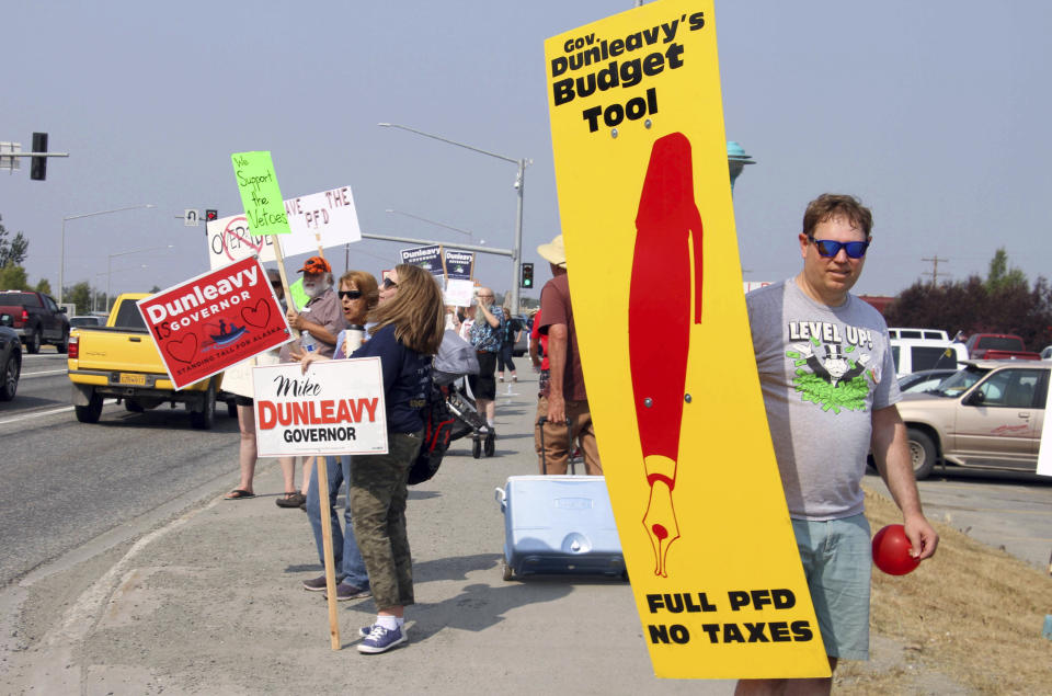 FILE - In this July 8, 2019 file photo, supporters of a fully funded oil check hold signs in Wasilla, Alaska. For decades, Alaska has had an uneasy reliance on oil, building budgets around its volatile boom-or-bust nature. When times were rough, prices always seemed to rebound, forestalling a day of reckoning some believe may finally have come. The situation has politicians weighing changes to the annual dividend paid to residents from earnings of the state's oil-wealth fund, the Alaska Permanent Fund. (AP Photo/Mark Thiessen, File)