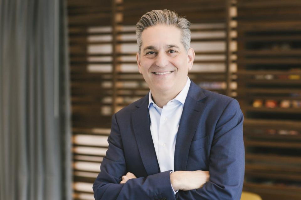 Headshot of Cresset cofounder Eric Becker wearing a white shirt and a navy suit in front of a shuttered window.