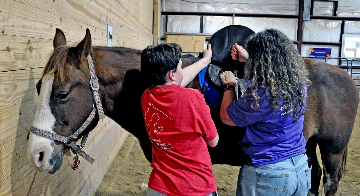 Carsen Klintworth gets help from his mother, Michelle, a volunteer, in putting a saddle on Pistol, a 20-plus-year-old therapy horse at Stirrup Courage.
