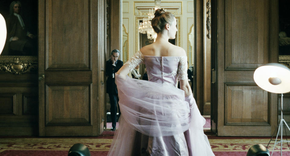 A woman in a fancy dress poses while a man looks on disapprovingly