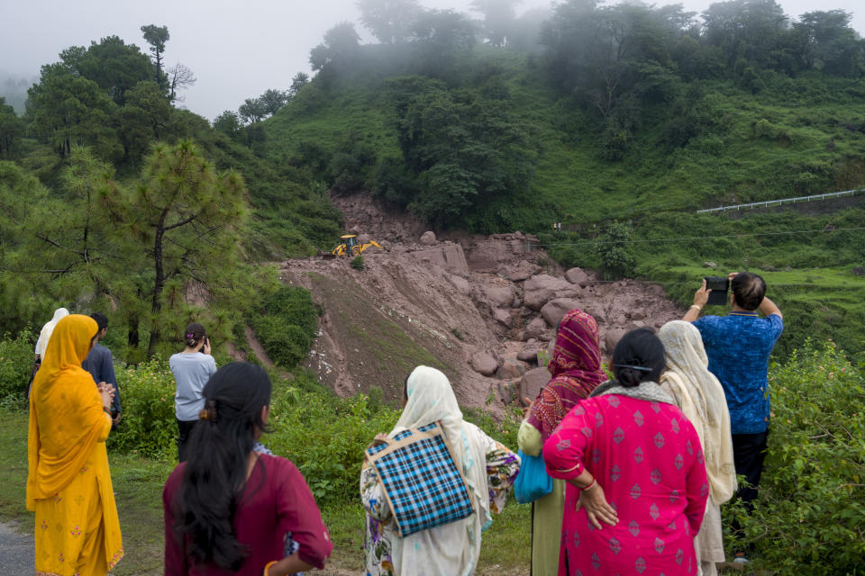 People watch an earth-mover being used to remove the debris after a landslide damaged part of a road near Dharamshala, India, Monday, Aug. 14, 2023. Heavy monsoon rains triggered floods and landslides in India's Himalayan region, leaving several people dead and many others trapped. (AP Photo/Ashwini Bhatia)