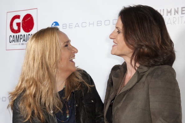 Melissa Etheridge and Linda Wallem sharing a laugh at a Go Campaign event. Melissa is wearing a black jacket and Linda is wearing a green blazer