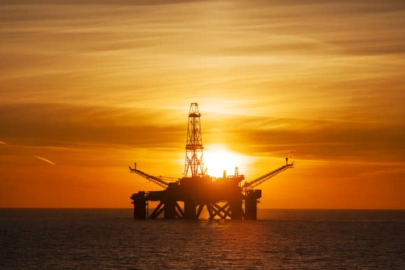 An offshore driling rig with the sun setting in the background.