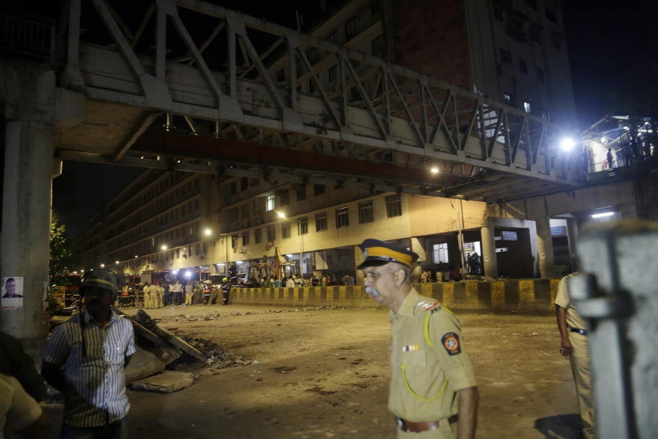 A policeman walks past a pedestrian bridge that collapsed in Mumbai, India, Thursday, March 14, 2019. A pedestrian bridge connecting a train station with a road collapsed in Mumbai on Thursday, killing at least five people and injuring more than 30, police said. (AP Photo/Rajanish Kakade)