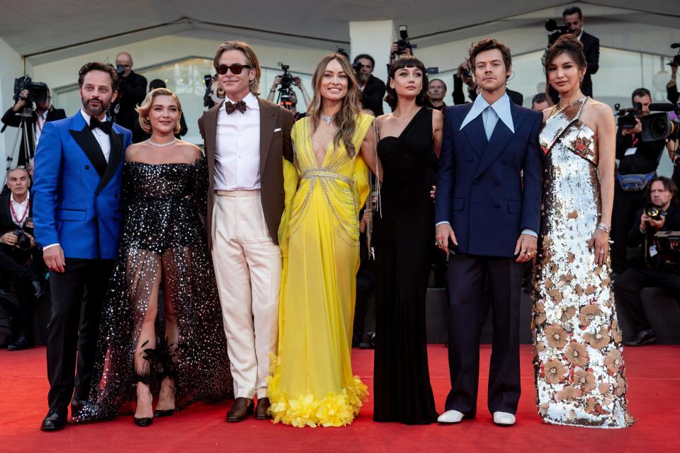 The cast of "Don't Worry, Darling," including Florence Pugh in a black dress, Olivia Wilde in a yellow gown, and Harry Styles in a navy blue suit, on the red carpet at the Venice Film Festval for the movie's premiere.