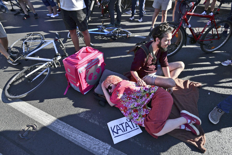 A demonstrator rests during an anti-government protest, in Budapest, Hungary, Monday, July 18, 2022. Anti-government demonstrators in Hungary blocked one of the capital's main thoroughfares during morning rush-hour traffic Monday, the latest in a series of protests against recent changes to the country's tax code that have carried on for nearly a week. Writing on sign is the acronym for the tax law being changed. (AP Photo/Anna Szilagyi)