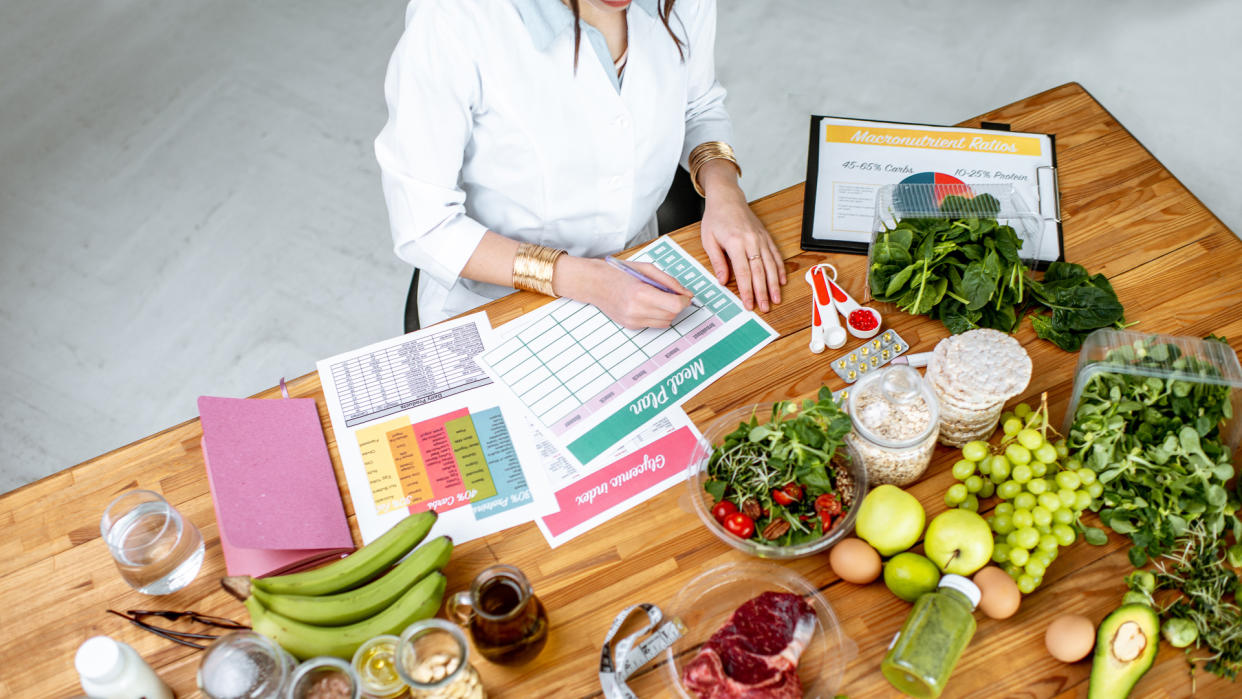 Dietitian writing a diet plan, view from above on the table with different healthy products and drawings on the topic of healthy eating.