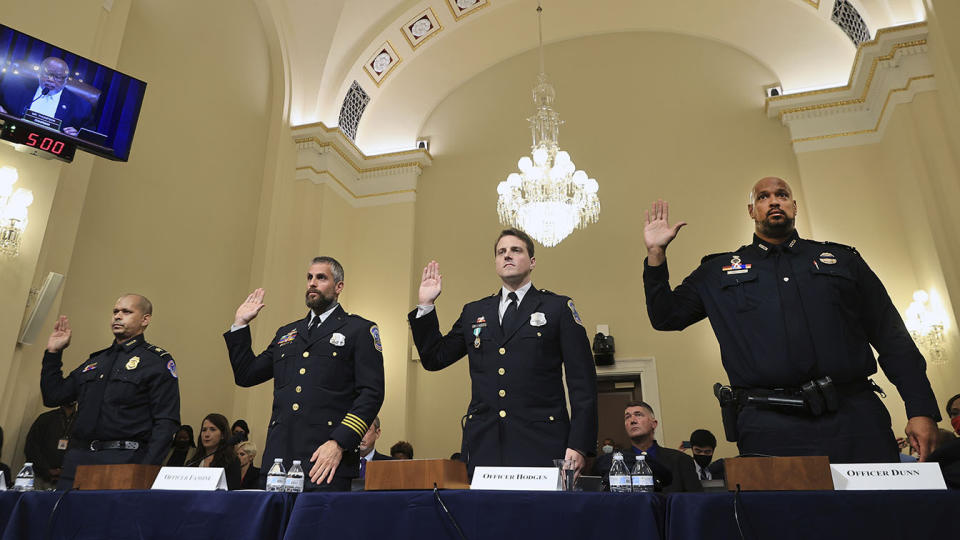 Officers Aquilino Gonell, Michael Fanone, Daniel Hodges and Harry Dunn stand with their right hands raised behind a table with microphones and placards bearing their names.