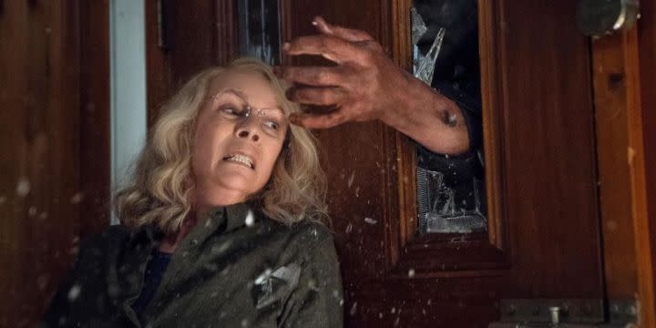 Jamie Lee Curtis hides behind a door in "Halloween" (2018).