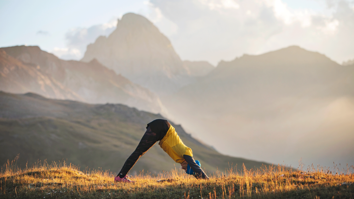 Hiker in the mountains practicing stretches for athletes, including Downward-Facing Dog