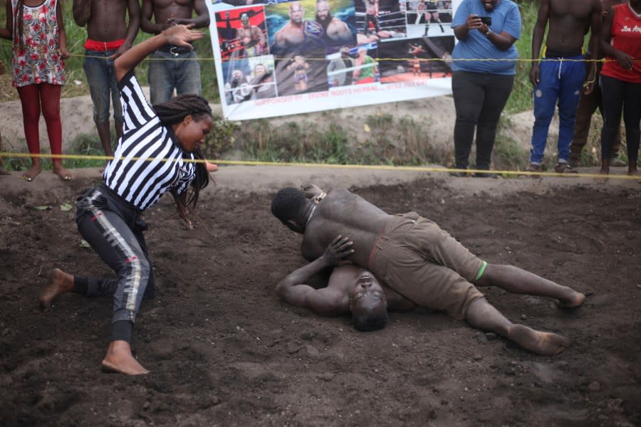 Ugandan youths perform an amateur wrestling tangle in the soft mud in Kampala, Uganda Wednesday, March. 20, 2023. The open-air training sessions, complete with an announcer and a referee, imitate the pro wrestling contests the youth regularly see on television. While a pair tangles inside the ring, made with bamboo poles strung with sisal rope, others standing ringside cheer feints and muscular shows of strength. (AP Photo/Patrick Onen)