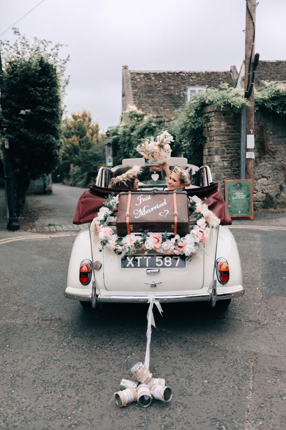 A couple rides in a white convertible that is decorated with "just married" on the back.