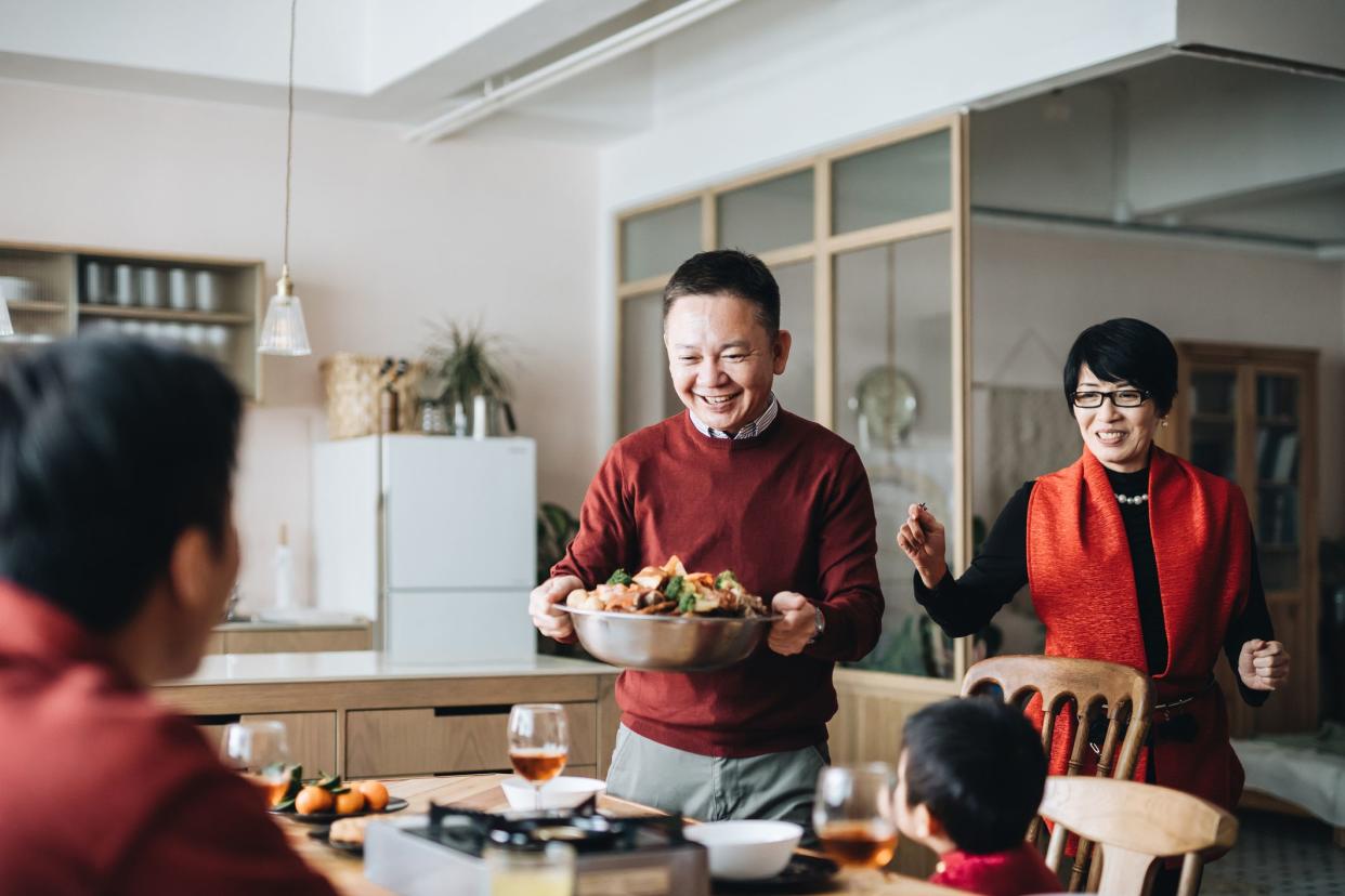 Three generations of joyful Asian family celebrating Chinese New Year and grandparents serving traditional Chinese poon choi on reunion dinner