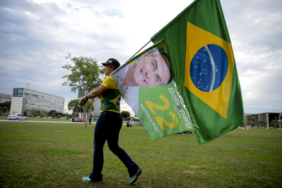 A woman holds a Brazilian flag and another with the image of Brazilian President Jair Bolsonaro, who is running for another term, after general election polls closed in Brasilia, Brazil, Sunday, Oct. 2, 2022. (AP Photo/Ton Molina)