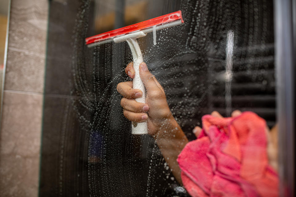 A hand using a squeegee to clean a glass surface with a pink cloth nearby