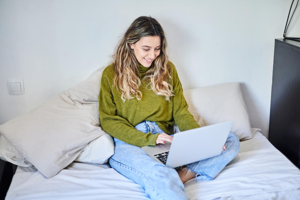 Young woman working with laptop computer on her bed at home.