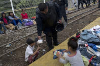 A Guatemalan police officer gives a migrant child some food as the migrants bound for the U.S.-Mexico border wait on a bridge that stretches over the Suchiate River, connecting Guatemala and Mexico, in Tecun Uman, Guatemala, early Saturday, Oct. 20, 2018. The migrants have moved about 30 feet back from the gate that separates them from Mexican police to establish a buffer zone. About 1,000 migrants now remain on the bridge between Guatemala and Mexico. (AP Photo/Moises Castillo)