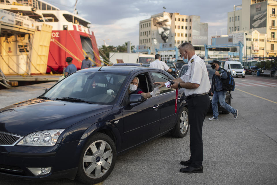 An employee wearing a face mask to reduce the spread of the coronavirus checks tickets of the vehicles as passengers embark a ferry at the Piraeus port near Athens on Monday, May 25, 2020. Greece restarted Monday regular ferry services to the islands as the country accelerated efforts to salvage its tourism season. (AP Photo/Petros Giannakouris)