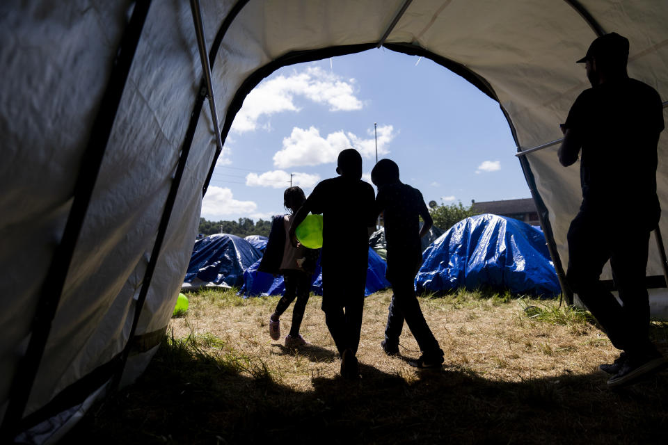 Children walk out of a community tent housing supplies and power at an encampment of asylum-seekers mostly from Venezuela, Congo and Angola next to an unused motel owned by the county, Wednesday, June 5, 2024, in Kent, Washington. The group of about 240 asylum-seekers is asking to use the motel as temporary housing while they look for jobs and longer-term accommodations. (AP Photo/Lindsey Wasson)