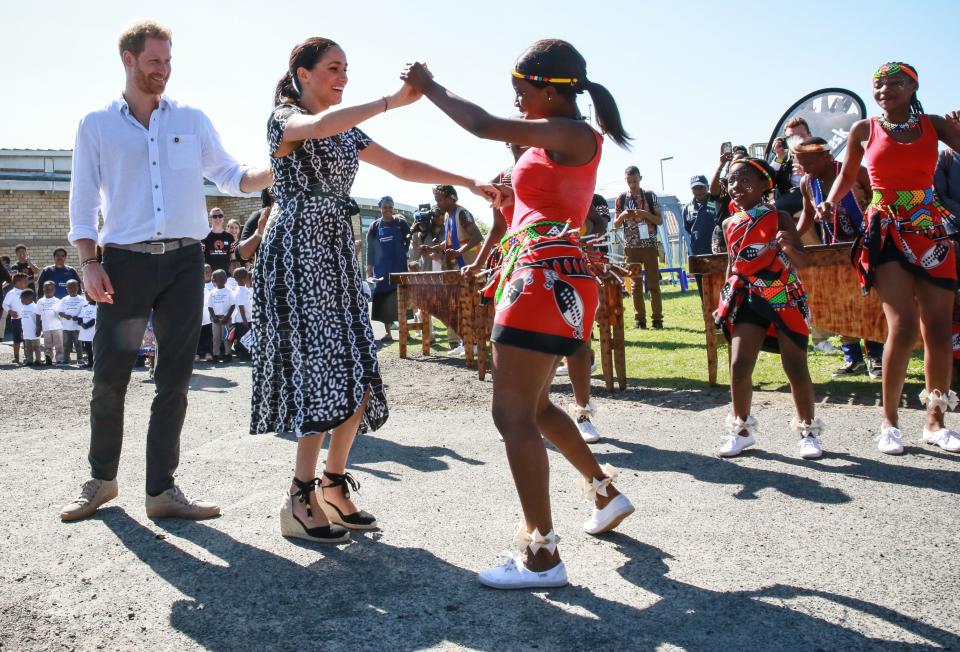 Prince Harry, Duke of Sussex and Meghan, Duchess of Sussex dance as they arrive for a visit to &quot;Justice  desk&quot;, an NGO in the township of Nyanga in Cape Town, as they begin their tour of the region on September 23, 2019. - Britain's Prince Harry and his wife Meghan arrived in South Africa on September 23, launching their first official family visit in the coastal city of Cape Town. The 10-day trip began with an education workshop in Nyanga, a township crippled by gang violence and crime that sits on the outskirts of the city. (Photo by Betram MALGAS / POOL / AFP)        (Photo credit should read BETRAM MALGAS/AFP/Getty Images)