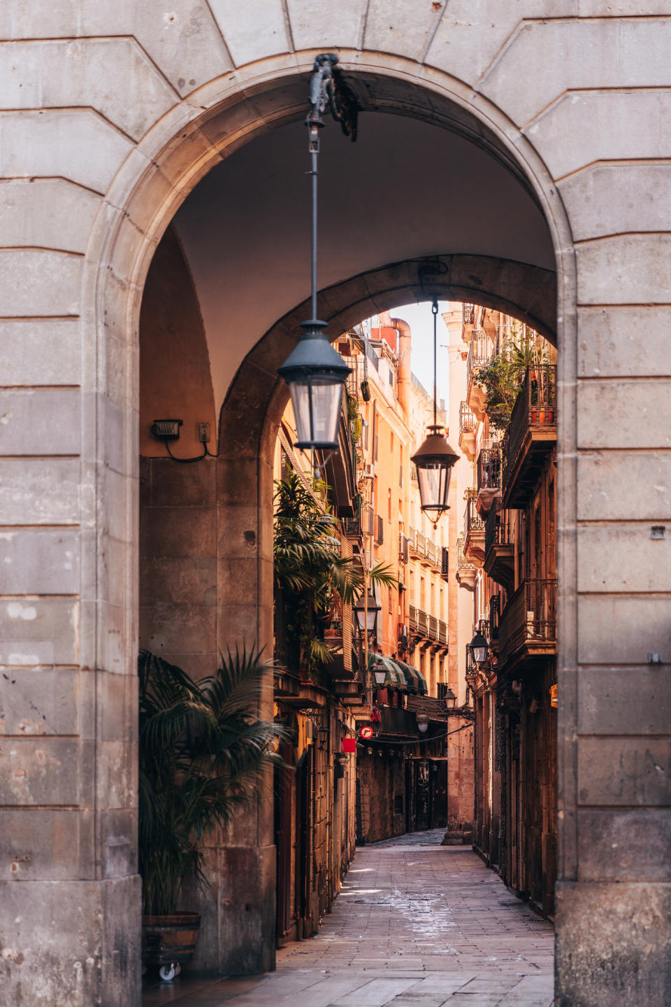 Arched stone doorway opening to a narrow street with hanging lamps and buildings on either side