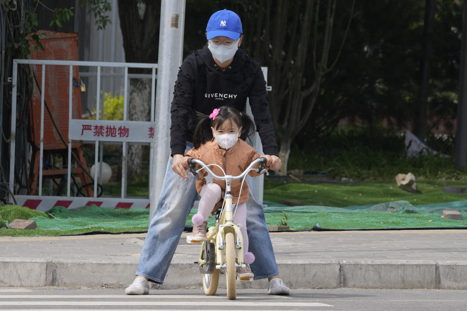 A woman and child wearing masks cross a road on Monday, May 9, 2022, in Beijing. (AP Photo/Ng Han Guan)